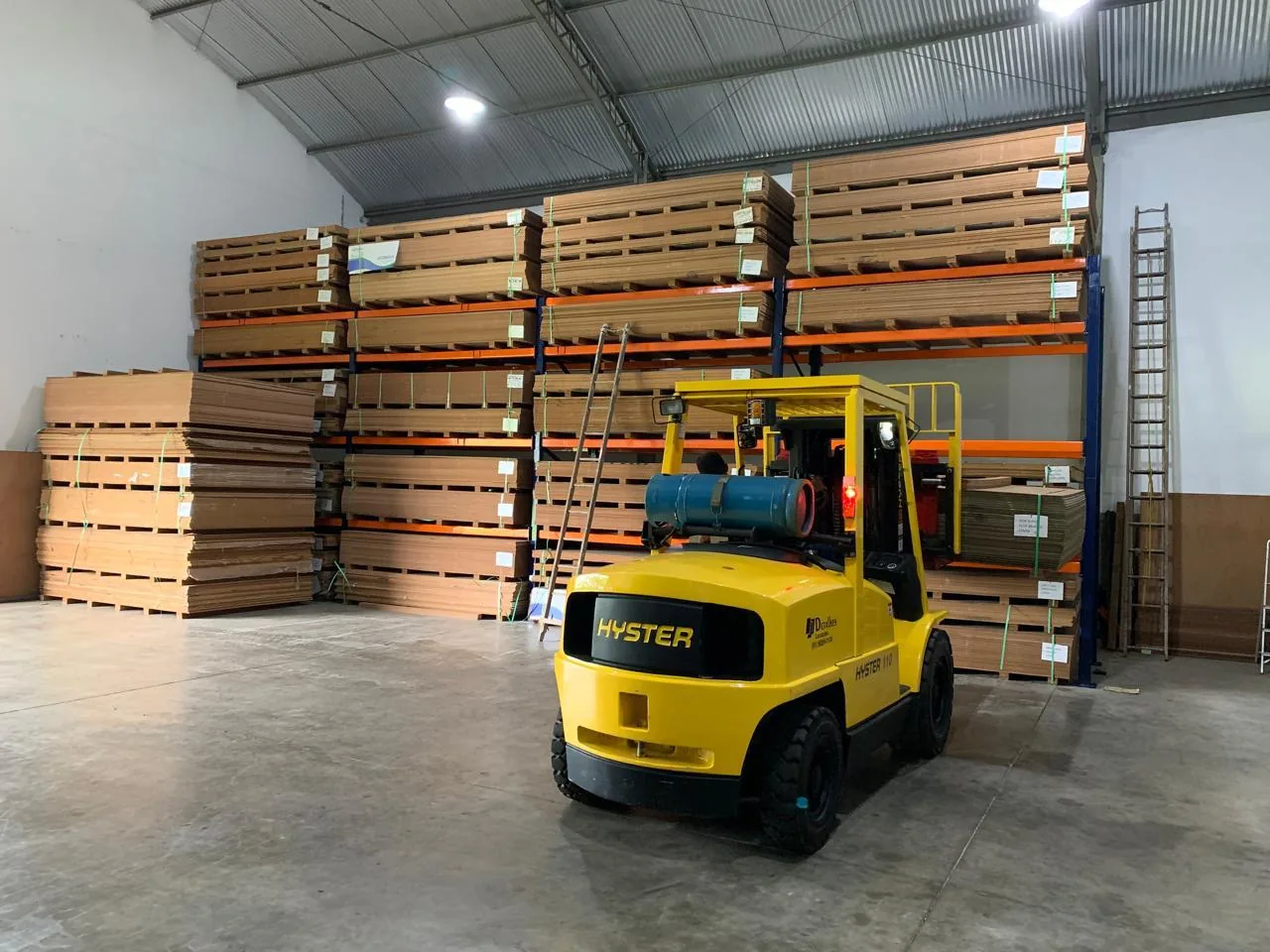 Operação logística no estoque da Detalhes MDF, com empilhadeira movimentando chapas